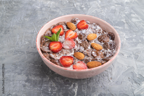 Chocolate cornflakes with milk, strawberry and almonds in ceramic bowl on gray concrete background. Side view.