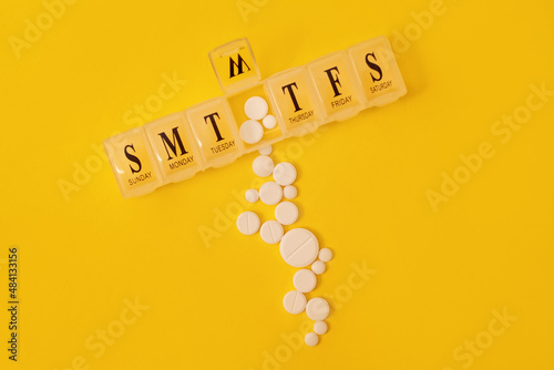 Medical pills in pill organizer on yellow background. Daily pill box with medications. Medicne concept