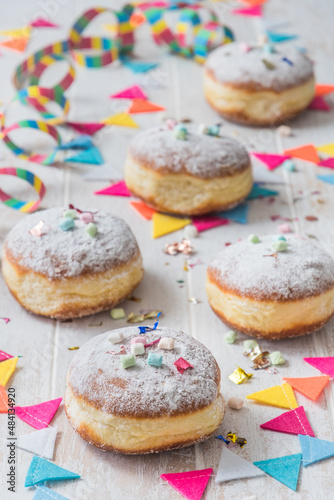 Krapfen, Berliner or donuts with streamers, confetti and mini marshmallows on white wooden background. Colorful vertical carnival or birthday image.