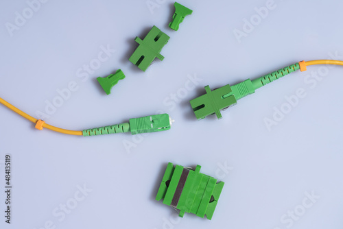 Optical patch cords with SC-APC connector, one patch cord adapter inserted, single and double SC-APC adapters lie nearby, light background photo