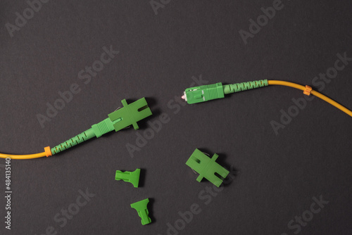 Two optical patch cords with an SC-APC connector, an adapter is put on the second patch cord, an additional SC-APC adapter is nearby, a dark background