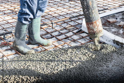 Construction worker leveling a poured concrete floor in an industrial workshop. Legs in boots in concrete. Surface concreting. Monolithic reinforced concrete works.