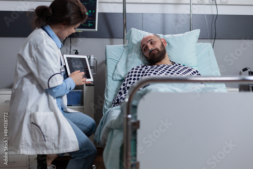 Doctor holding digital tablet with brain mri pointing at results indicating tumor explaining treatment options to patient. Middle aged man recieving diagnosis while connected to oxygen dispenser. photo