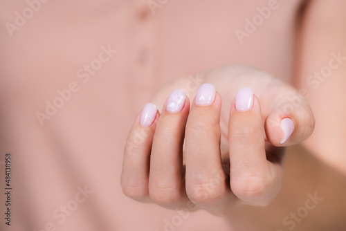 Closeup top view of elegant pastel pink natural manicure. Horizontal color photography of manicured female hands with holiday Valentines day or wedding nail design. Pink nails with white hearts