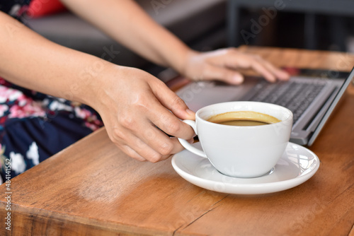 Close-up view of woman hand hold white coffee cup with laptop.