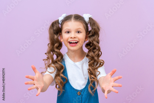 The joyful baby stretched out her hands and asked for something. Please give me a thing. A child with long curly hair on an isolated background.