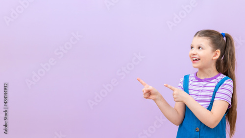 Child points his fingers at the advertisement. A little girl in a denim dress on an isolated background.