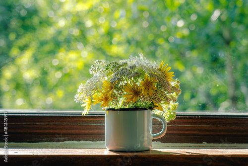 Home cozy simple decorations of house with spring or sumemr cute field flowers. Bunch of wild plants in blue metal mug standing on windowsill photo