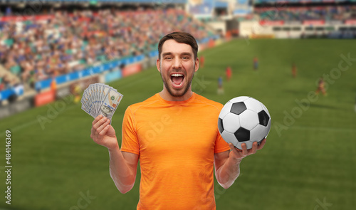 sport, leisure games and online betting concept - happy smiling man or football fan with soccer ball and money over stadium background