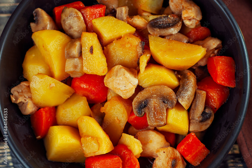 Boiled potatoes with meat in a black bowl. Potatoes with mushrooms and carrots. Boiled mushrooms and chicken with potatoes. Food on a black wooden table. Boiled potatoes with meat in a black bowl. Potatoes with mushrooms and carrots. Boiled mushrooms and chicken with potatoes. Food on a black wooden table.