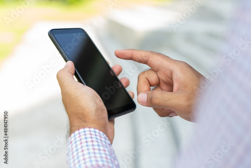 Close up businessman using modern smartphone device typing text message in social media while sitting on stairs outdoor. Happy male spending free time in break of working.