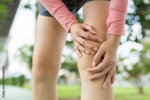 A young woman in sports outfits pink injured her knee during exercise in the park. Low section of sports girl suffering from joint pain while standing on track during. Accident from exercise concept.