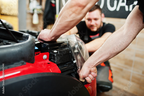 Car service worker put anti gravel film on a red car body at the detailing vehicle workshop. Car protection with special films.