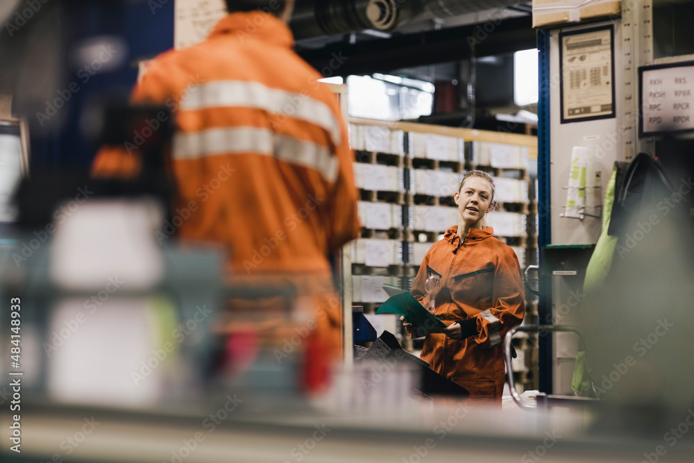 Female worker in uniform discussing with male coworker in factory Female worker in uniform discussing with male coworker in factory