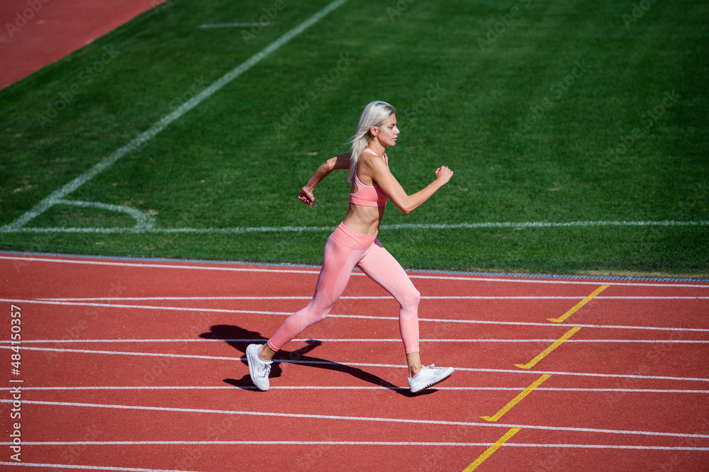 Great progress. woman sport trainer in motion. speed and energy. stamina. sexy runner in fitness sportswear. sprinting on outdoor arena racetrack. training and workout. athletic female coach running