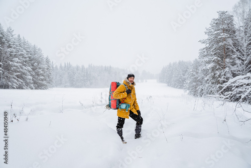 Smiling and happy traveler with hiking backpack on the back. Snowy forest and rocks. Climbing the mountain in winter. Survival in the wild.