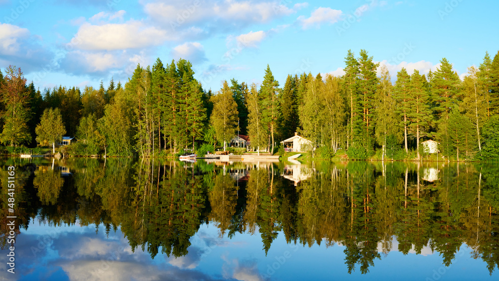 Fototapeta premium Wunderschöner Blick auf Stukas Ferienhäuser vom See aus in Schweden mit Spiegelungen im Wasser vom Boot aus Im Schwedenurlaub