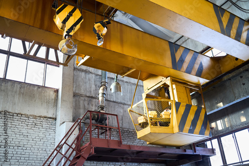 Yellow with black stripes overhead crane with linear traverse and hooks at petrochemical enterprises chemical plant workshop. Crane operator cabin and hooks and jib crab trolley. Landing staircase. photo