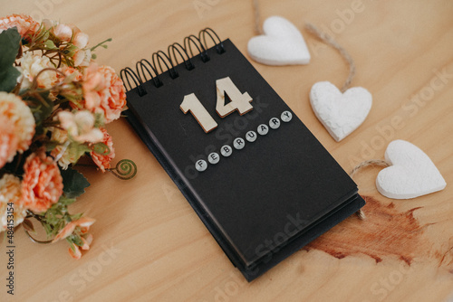 Wooden calendar on February 14 with roses and heart.