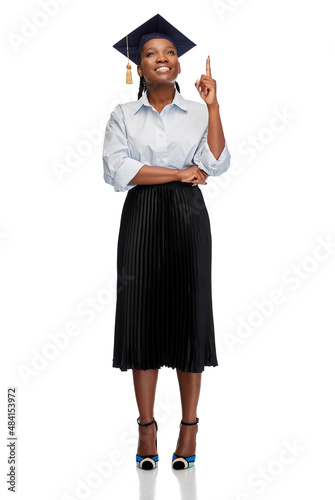 education, graduation and people concept - happy graduate student woman or bachelor in mortarboard pointing finger up over white background