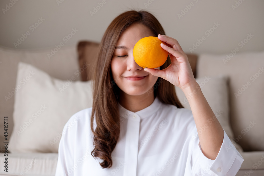 Closeup image of a young woman holding and covering eye with an orange Closeup image of a young woman holding and covering eye with an orange
