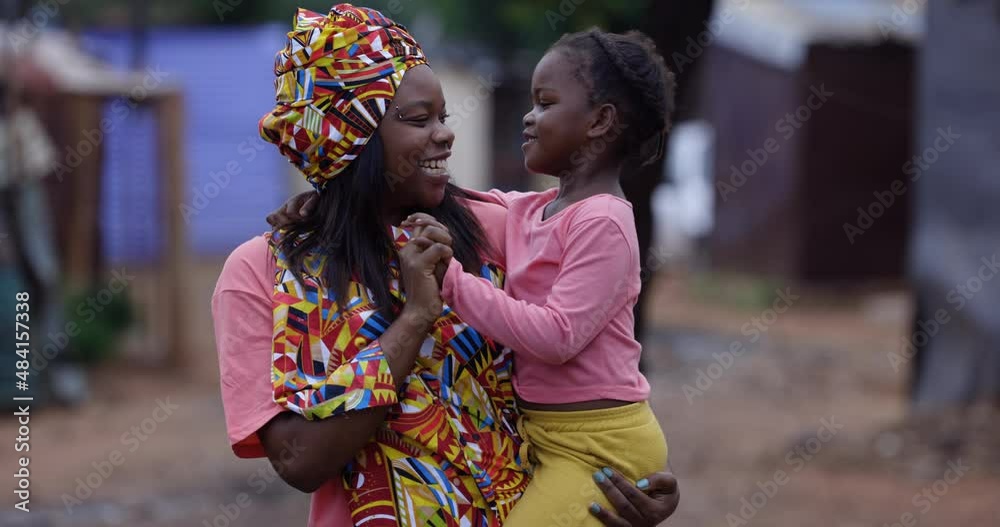 Close-up.Black African woman in traditional clothing holding and interacting with her cute daughter in an informal settlement slum