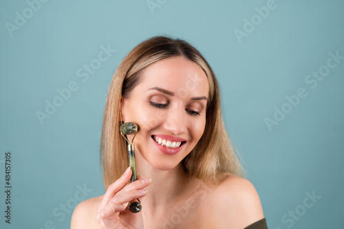 Close up beauty portrait of a woman with perfect skin and natural make-up, plump nude lips, holding a roller massager for face and neck.