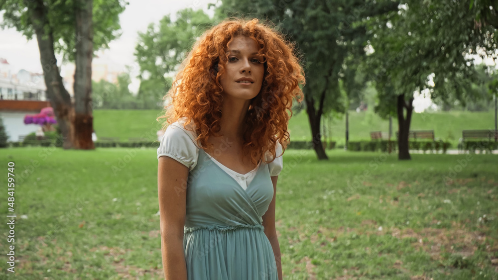pretty redhead woman looking at camera while standing in park. pretty redhead woman looking at camera while standing in park.