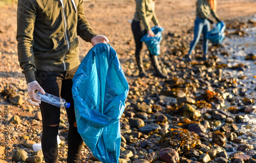 Close-up of man collects garbage in bag with group of volunteers on sunny day