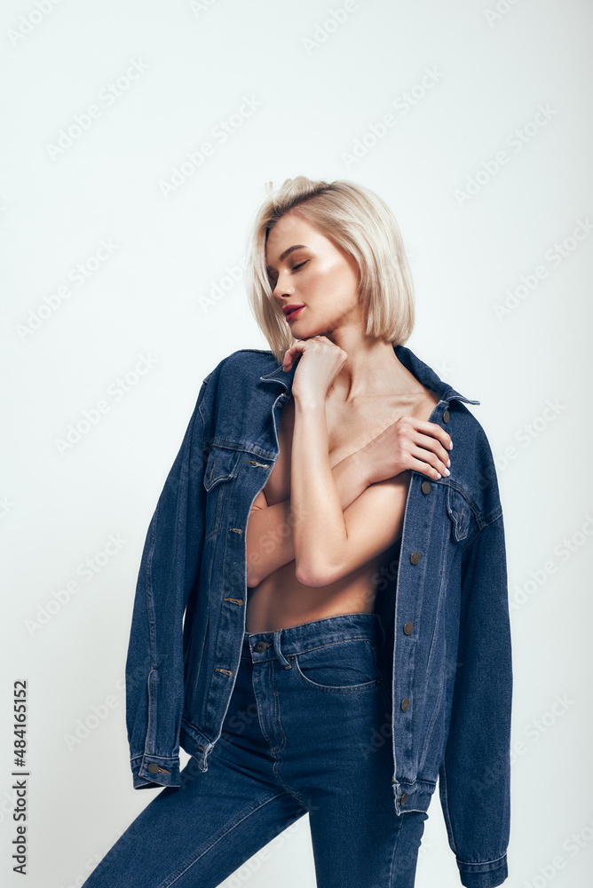Great look. Sexy young woman in jeans wear keeping eyes closed while standing against grey background in studio Great look. Sexy young woman in jeans wear keeping eyes closed while standing against grey background in studio