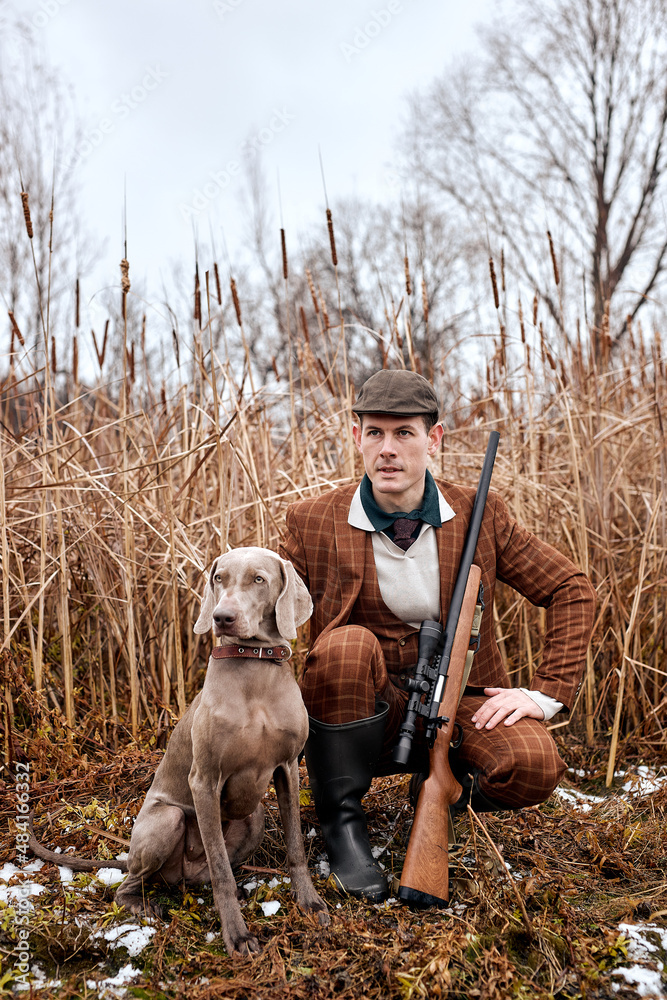 Handsome hunter male hunt on ducks and wild animals in autumn, in nature. friendly Dog help him to hunt, sit together among grass, male with rifle shotgun, ready for hunting, in countryside