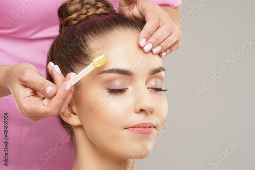 Beautician is removing hair from young female face with hot wax. Woman has a beauty treament procedure. Depilation, epilation, skin and health care concepts.