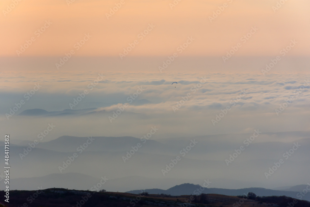 Pastel pink sunset mountains. Gentle blurred natural atmospheric background. Fog low clouds paraglider in the distance. Fabulous beige-pink dawn light. Calm landscape, copy space. Travel concept