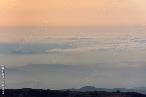 Pastel pink sunset mountains. Gentle blurred natural atmospheric background. Fog low clouds paraglider in the distance. Fabulous beige-pink dawn light. Calm landscape, copy space. Travel concept
