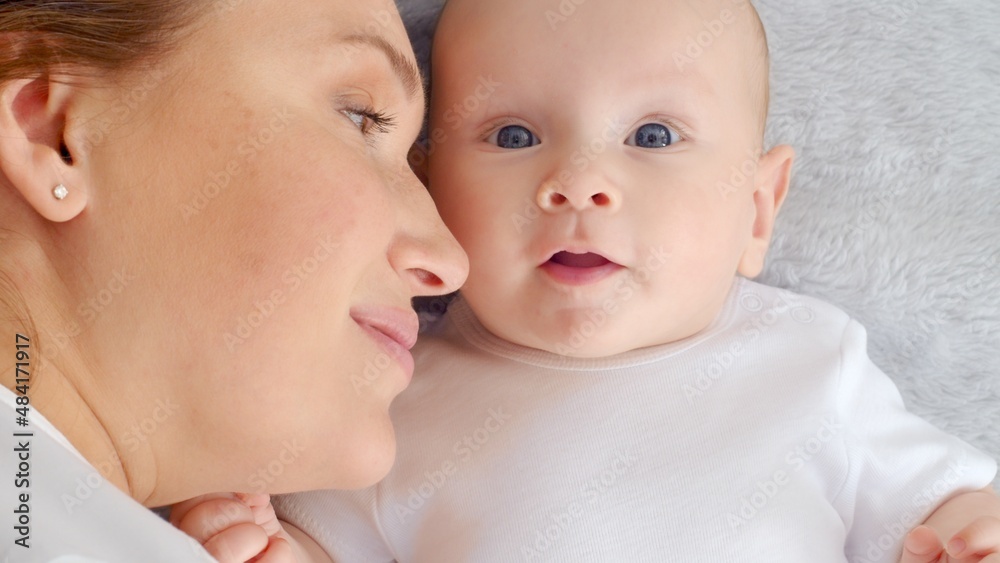 Happy newborn baby with his mother. Healthy newborn baby in a white t-shirt with mom. Closeup Faces of the mother and infant baby. Cute Infant boy and parent, top view. Happy family portrait Happy newborn baby with his mother. Healthy newborn baby in a white t-shirt with mom. Closeup Faces of the mother and infant baby. Cute Infant boy and parent, top view. Happy family portrait