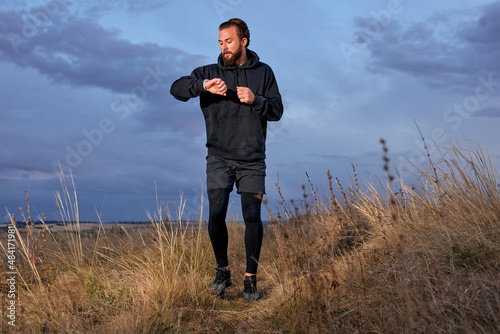 sportsman checking the time on smart wristwatches while jogging on sunrise in the morning outdoors in nature, sport on fresh air, training workout. young caucasian guy in black sportive outfit © alfa27