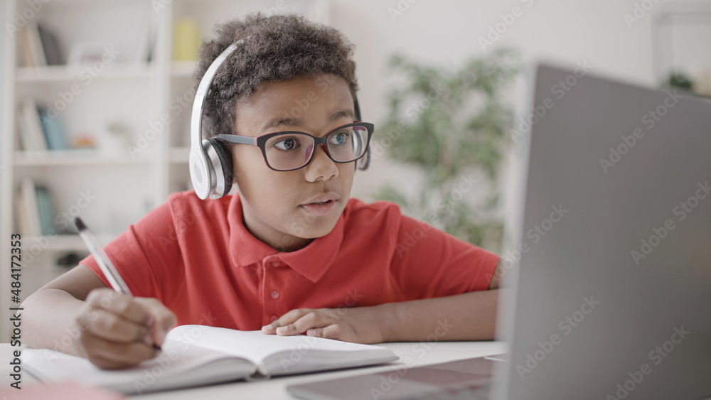 Black school pupil looking at laptop display and writing exercise in copybook, online lesson, school Black school pupil looking at laptop display and writing exercise in copybook, online lesson, school