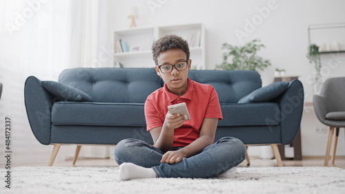 Bored African American boy scrolling smartphone, staying home during lockdown