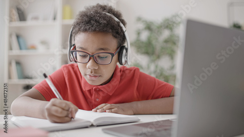 African american child writing exercise in copybook during online lesson, school