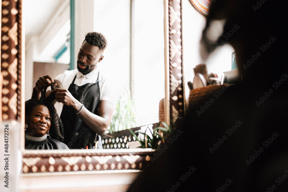 Male hairdresser making locs of female customer at barber shop Male hairdresser making locs of female customer at barber shop