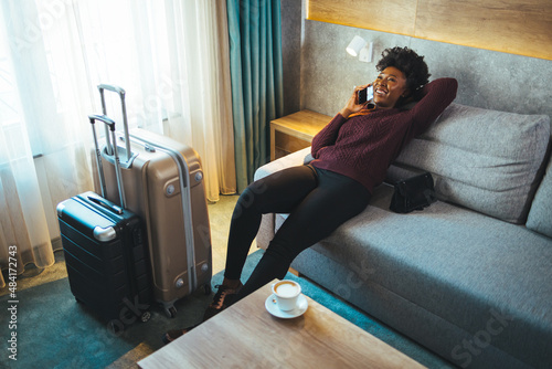 A shot of a happy adult woman sitting on her bed after closing her suitcase after she has finished packing for the vacation she is going on. Use your smartphone to book a trip.