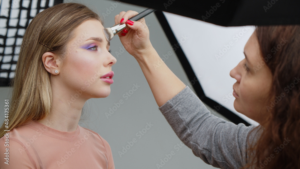 Backstage of the photo shoot: Make-up artist applies makeup on beautiful white  model. Tutorial makeup master class.