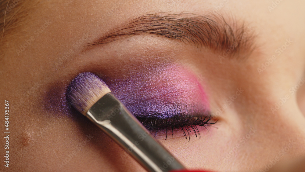 Make-up artist applies makeup to the upper eyelid, close-up.  Makeup artist applies a bright eye shadow with a makeup brush. Tutorial master class of professional makeup.