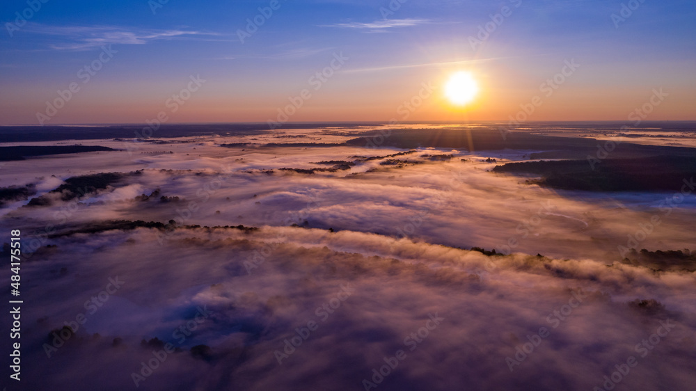 Aerial  view of a beautiful summer  landscape with a fog while dawn.  Photo from drone of a foggy landscape in spring. Top view to land while sunrise. Sun is above the horizon