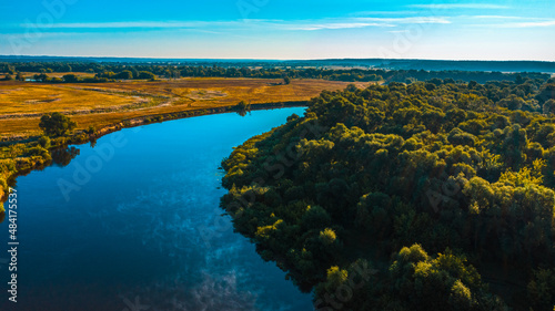 Aerial view of a beautiful summer landscape over river while dawn. Top view over river with a smooth water surface reflecting blue sky.