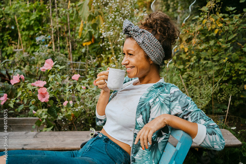 Smiling female farmer drinking coffee while sitting at urban farm