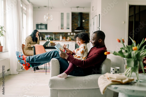 Smiling father teaching daughter sitting on chair in living room photo