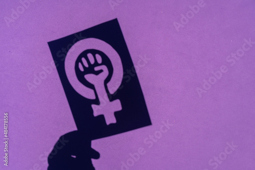 Shadow of the symbol of the fight for feminism on a purple background, clenched fist of a woman in the march protests for women's rights photo