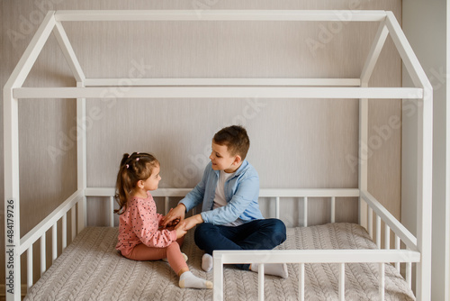 Two Children brother and sister are sitting in a Montessori bed and looking at each other.
