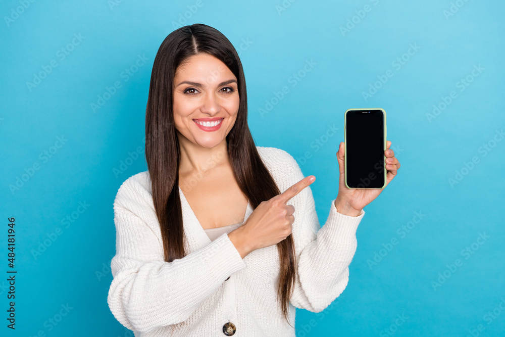 Photo of cheerful woman wear white cardigan pointing finger modern device empty space isolated blue color background Photo of cheerful woman wear white cardigan pointing finger modern device empty space isolated blue color background